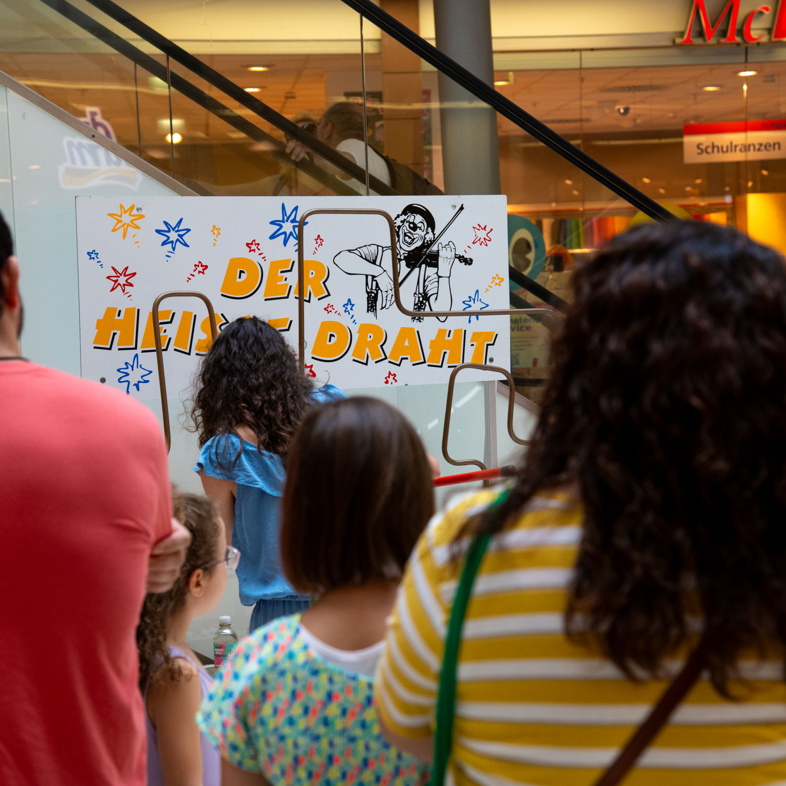Kinder und Erwachsene stehen vor einem Geschicklichkeitsspiel mit dem Titel „Der heiße Draht“.