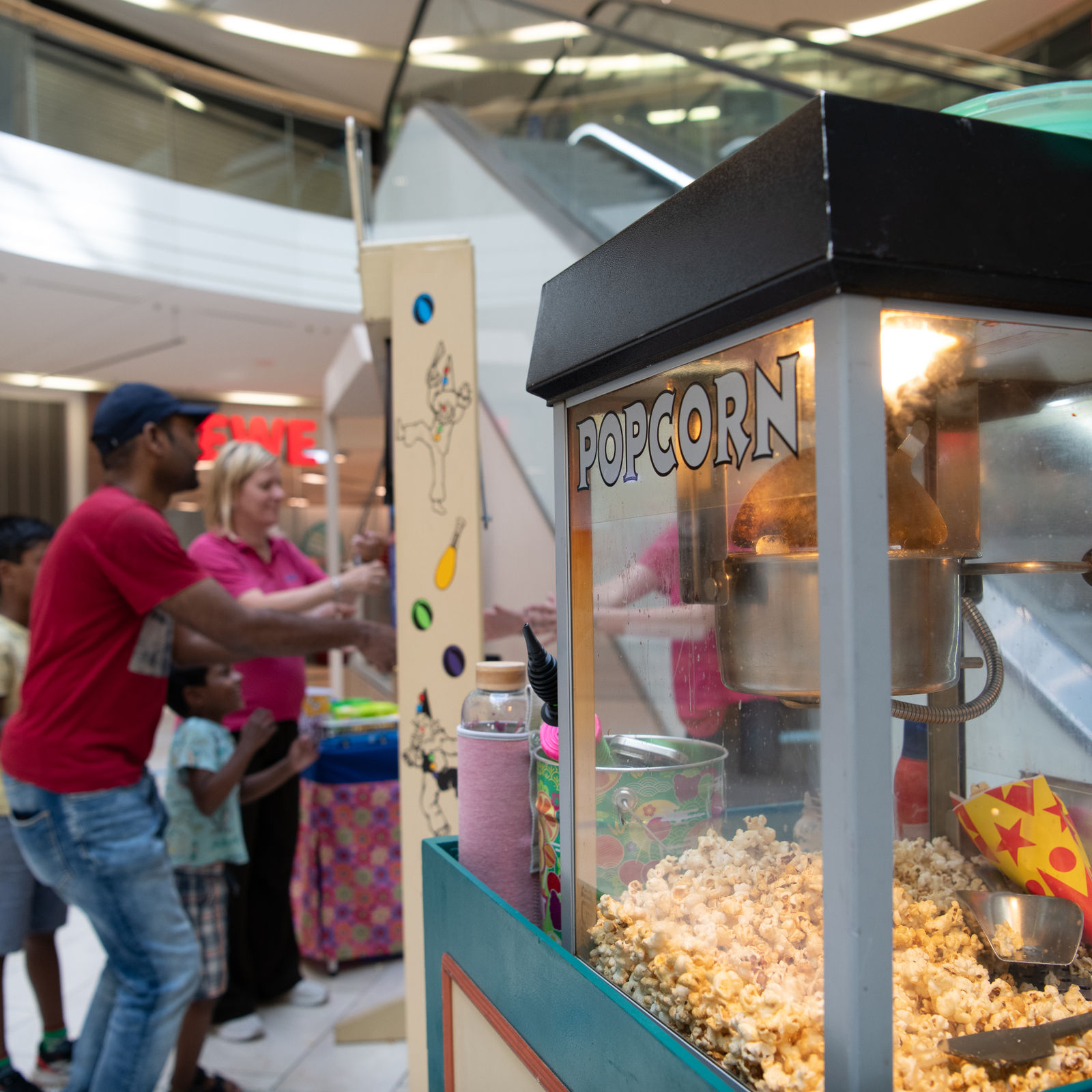Eine Popcornmaschine im Vordergrund, dahinter spielen Erwachsene und Kinder ein Spiel.