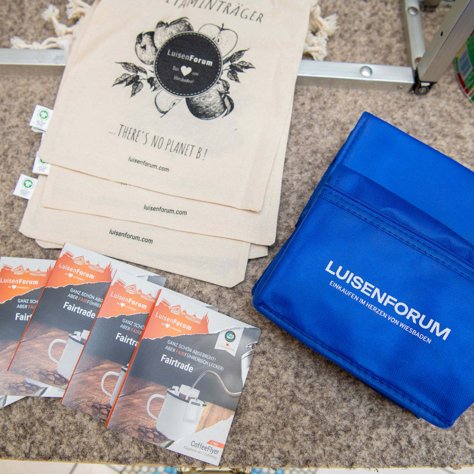 Giveaways wie Stoffbeutel, Fairtrade-Kaffeeproben und eine blaue Kühltasche mit LuisenForum-Logo.