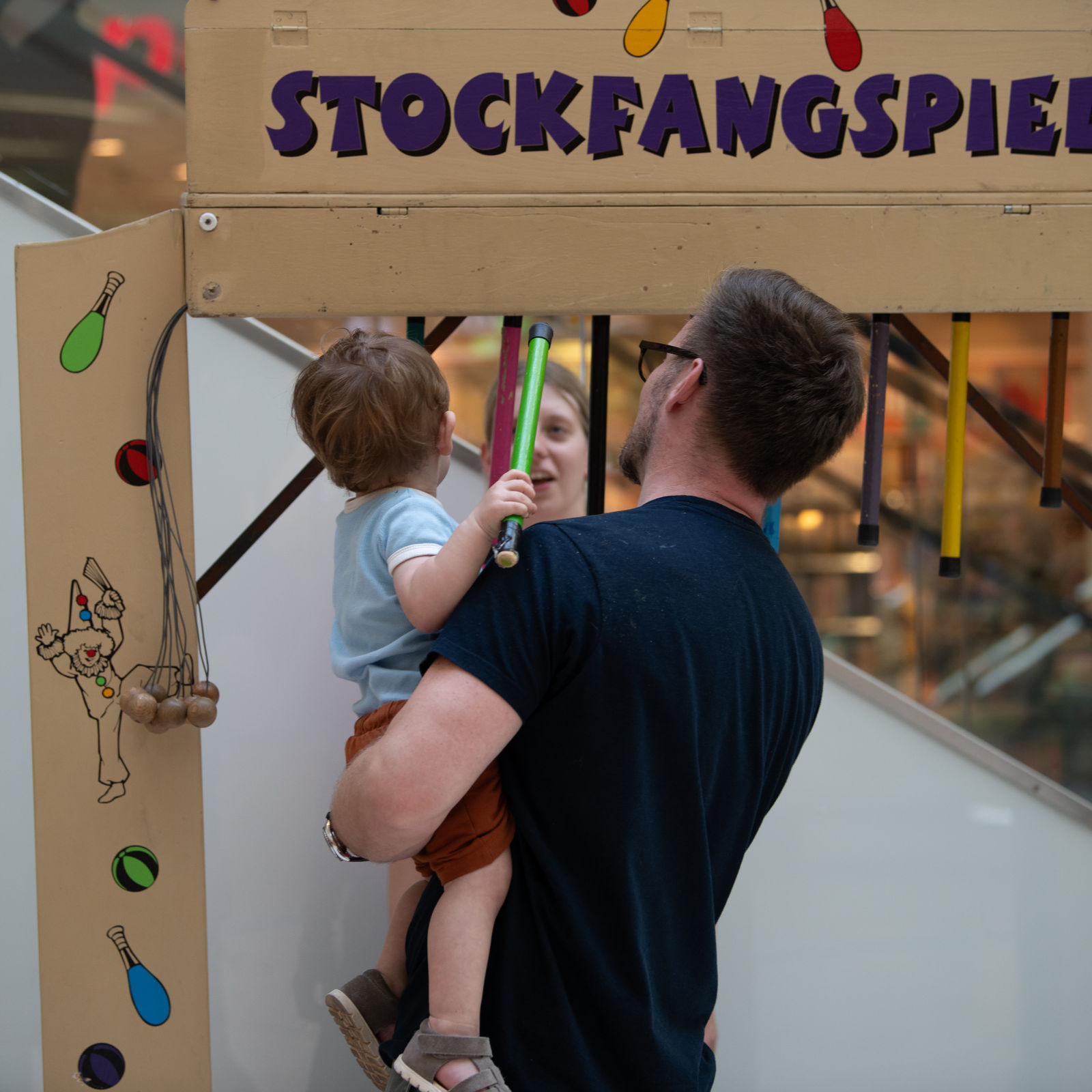 Ein Mann trägt ein Kleinkind auf dem Arm, beide spielen das Stockfangspiel.