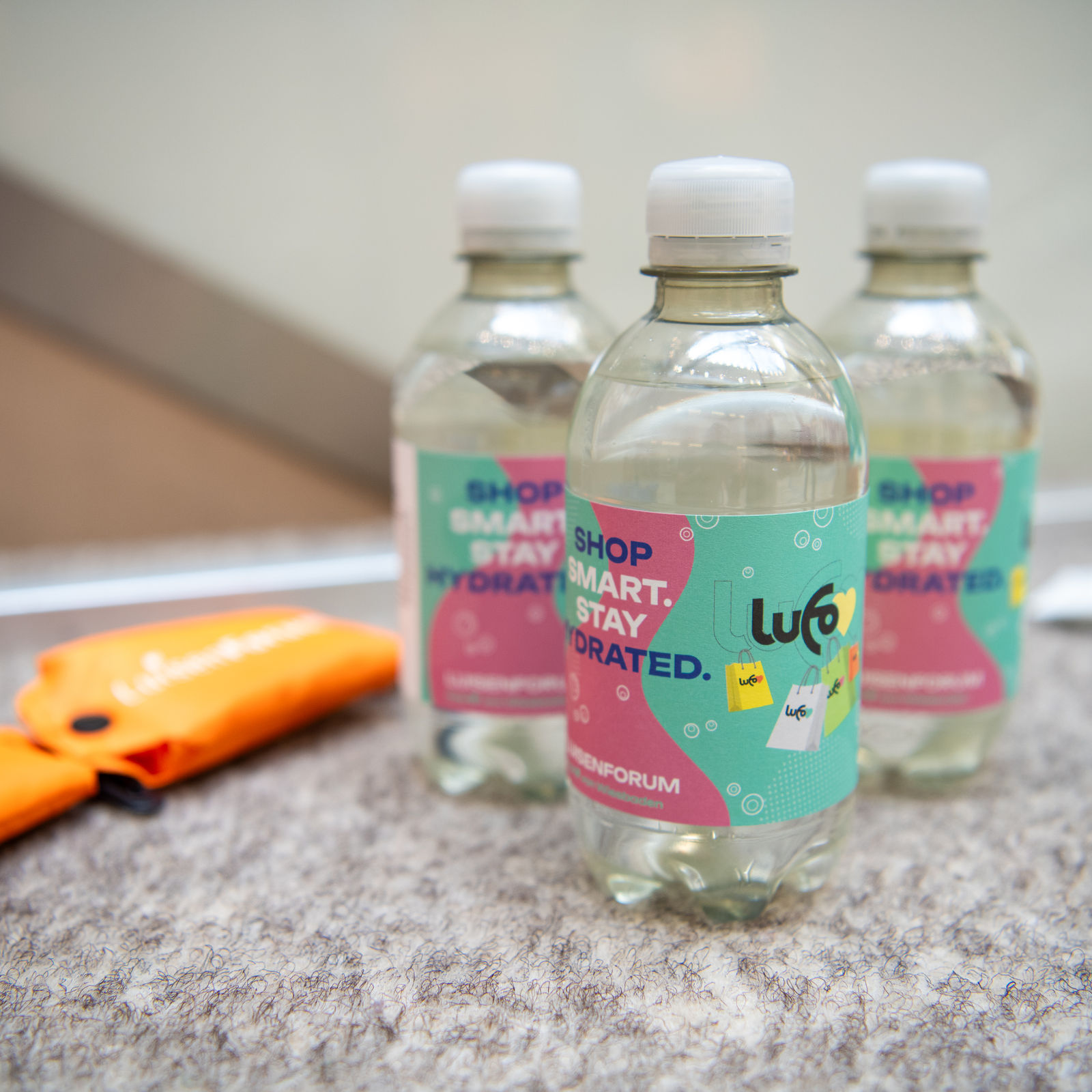 Drei Wasserflaschen mit LuisenForum-Etikett und der Aufschrift „SHOP SMART. STAY HYDRATED.“