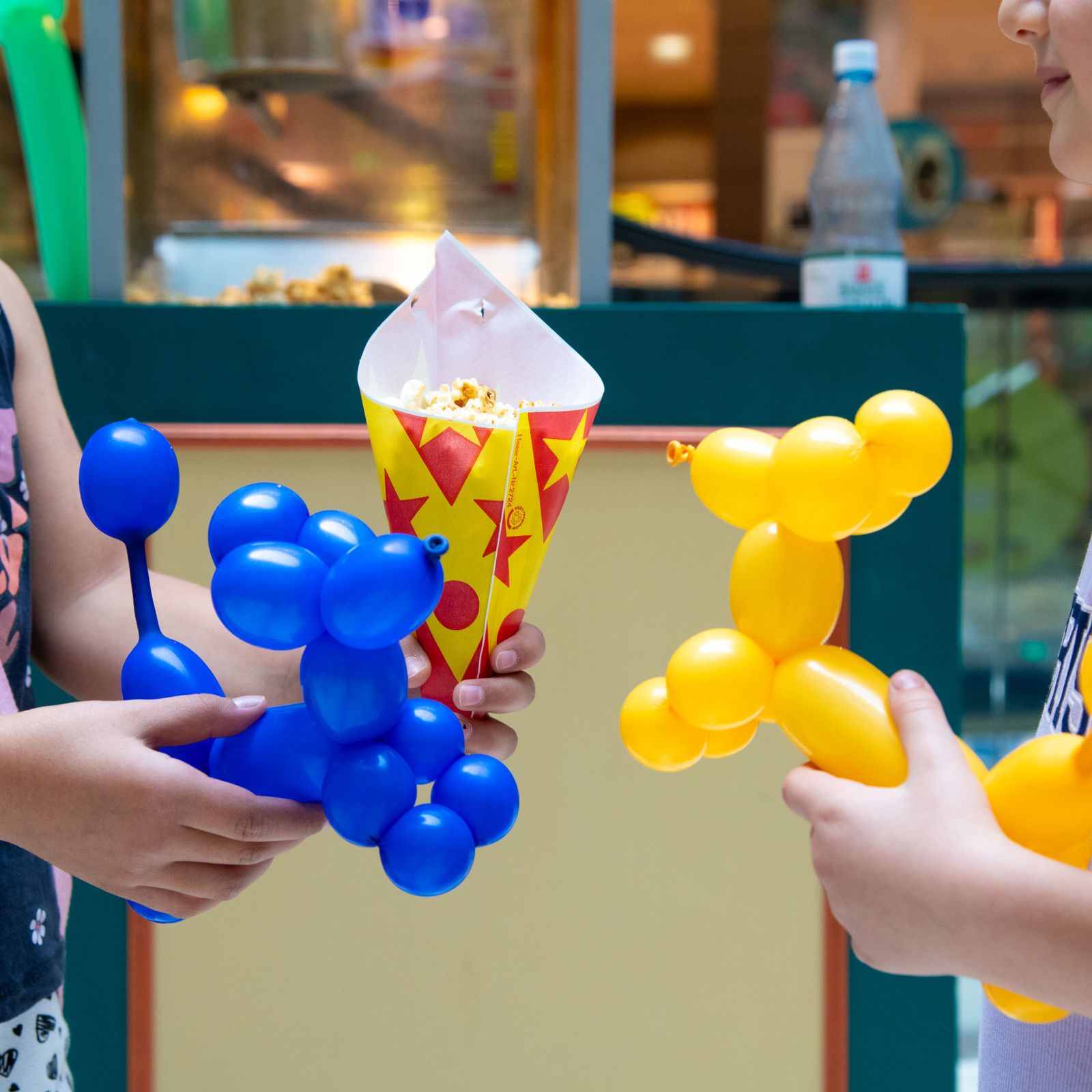 Zwei Kinder halten jeweils ein Luftballontier und eine Tüte Popcorn.